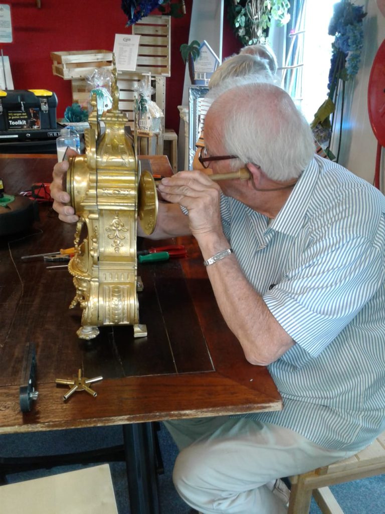 Klokkenmaker luistert met instrument naar de klok.
