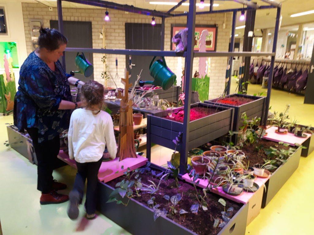 Juf geeft uitleg aan leerling over de binnentuin, verschillende plantenbakken met planten